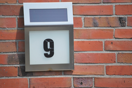 Eine beleuchtete Hausnummer an einer Wand mit einem Solarmodul oben drauf