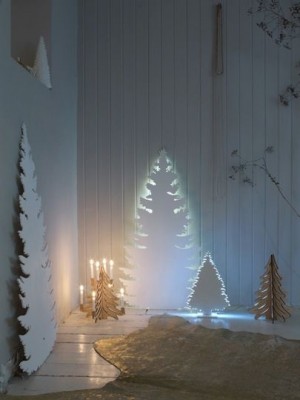 In einem dunklen Zimmer stehen weiße Weihnachtsbaum-Silhouetten an der Wand, die von hinten blau erstrahlen.