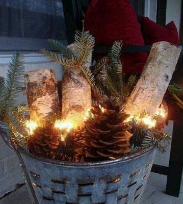 Ein Metallkorb, in dem Zweige, Äste und Zapfen liegen, ist zusammen mit einer Lichterkette darin eine schöne Weihnachtsbeleuchtung für Balkon oder Terrasse.