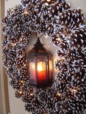 Ein winterlicher Kranz aus Kiefernzapfen, die von einer Lichterkette erleuchtet werden, hängt an der Tür.