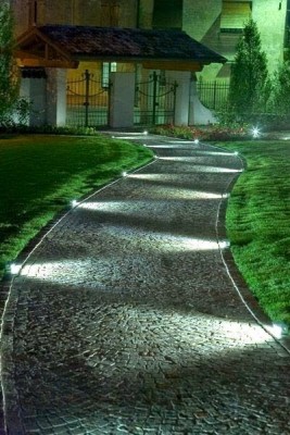 Ein Gartenweg wird in der Nacht mit Bodenspots erleuchtet, die waagerecht den Boden anstrahlen.