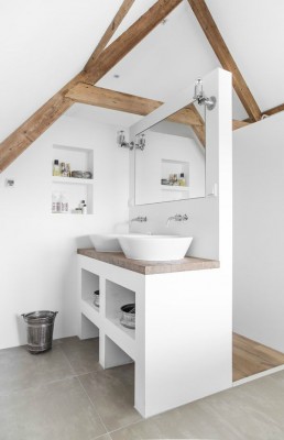 Ein helles Badezimmer mit Holzbalken und einem hölzernen Waschtisch sowie metallischen Armaturen und Spiegelleuchten.