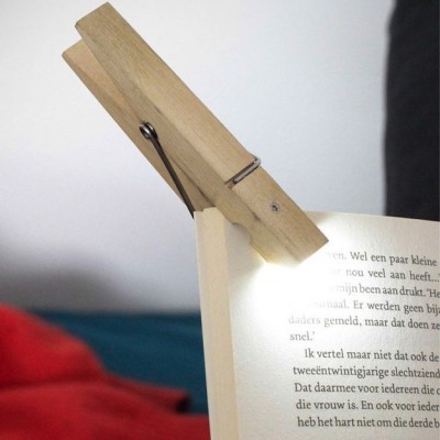 An einem aufgeschlagenen Buch klemmt in der linken oberen Ecke eine Klemmleuchte in Form einer Wäscheklammer.