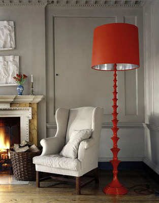 Eine Stehleselampe in knalligem Orange steht in einem in Beige- und Naturtönen gehaltenen Raum mit Kamin und Sessel