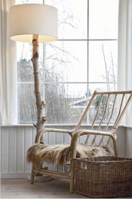 Eine Stehleselampe mit einem Holzstamm als Gestell steht neben einem Holzstuhl vor einem Fenster.