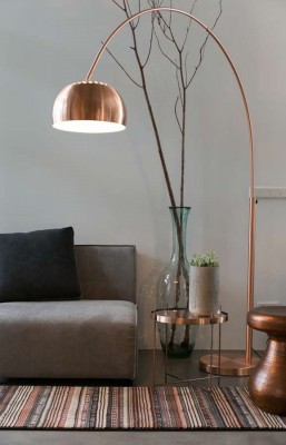 Eine Stehlampe mit gebogenem Hals aus Kupfer steht neben einem Sofa.