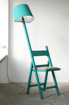 Eine türkise Stehleselampe mit einem integrierten Klappstuhl.
