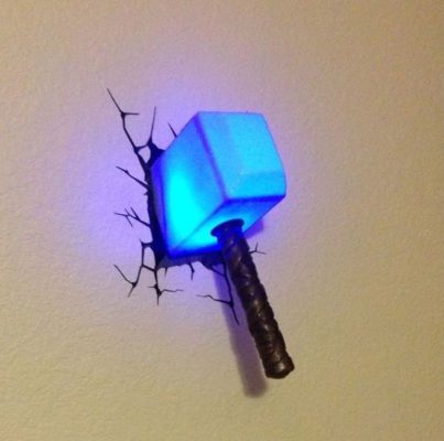 Ein mysthisch blau leuchtender Thors Hammer hängt als Leuchte an der Wand