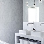 Ein hell gefliestes Bad mit einem eleganten Waschtisch aus Stein, vor den Spiegeln hängen zwei Deckenleuchten.