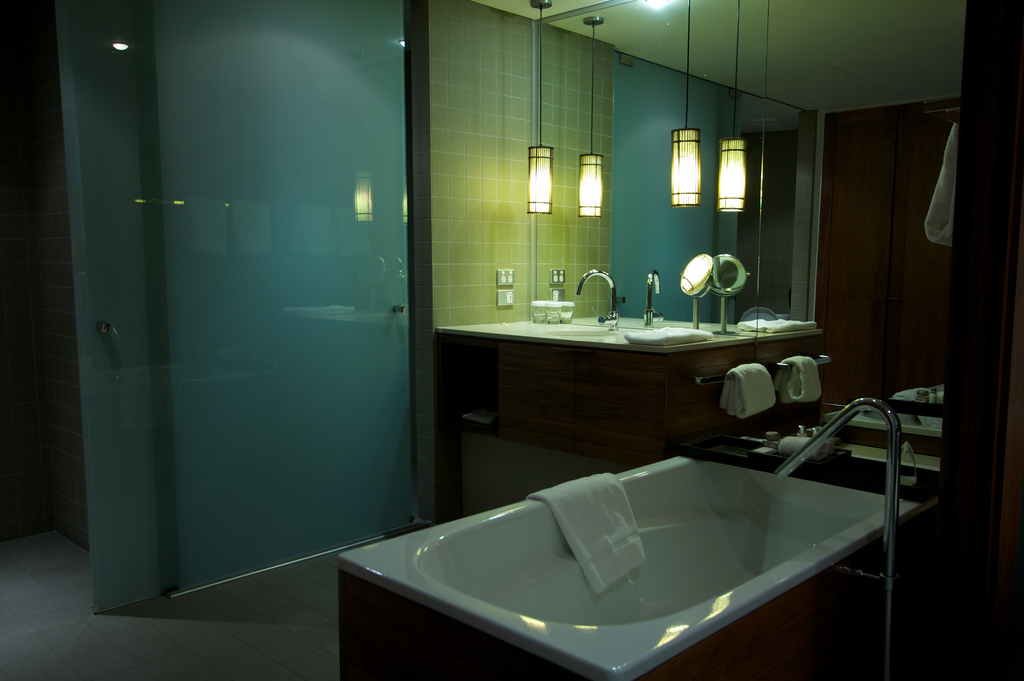 In einem modernen, blau gefliesten Badezimmer hängen zwei Spiegelleuchten von der Decke herab.