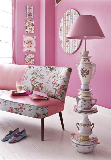In einem rosafarbenem Wohnzimmer neben einem Sofa mit Rosenstoff steht eine Stehleselampe aus Geschirr.