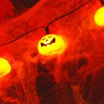 Eine Lichterkette aus kleinen Kürbissen taucht eine gruselige Halloween-Deko in orangefarbenes Licht.