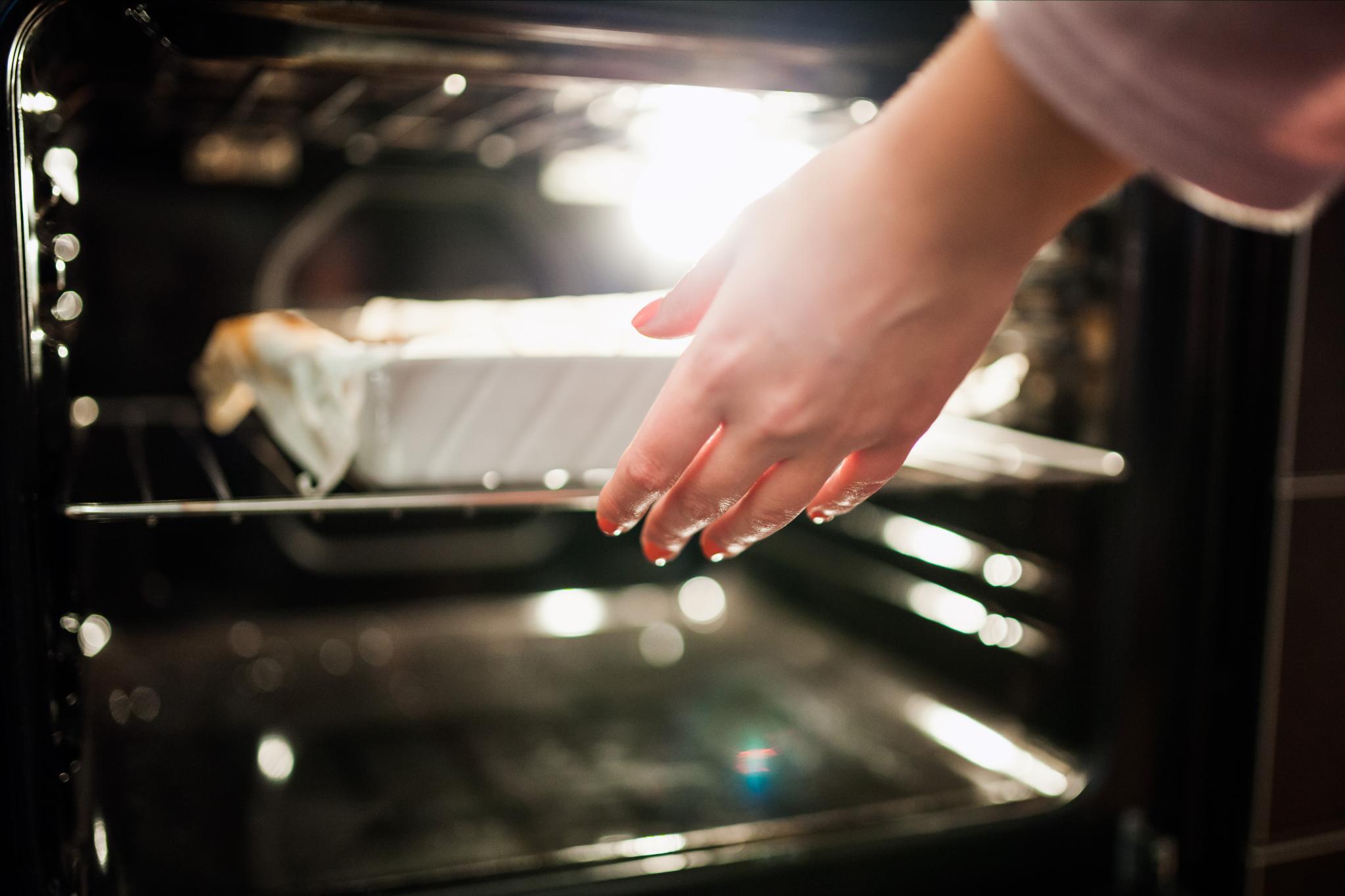 Eine Hand, die einen Auflauf in den Ofen schiebt, während die Backofenlampe leuchtet