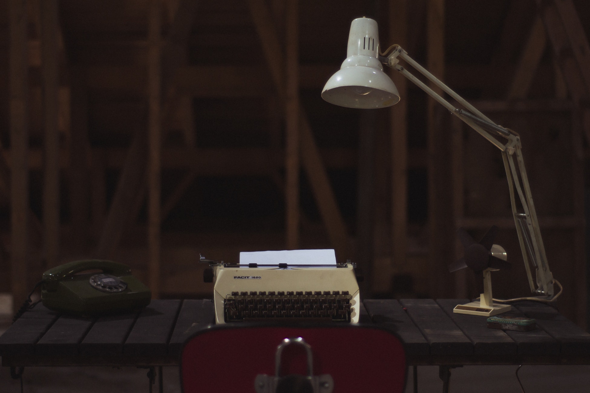 Die Kultlampe Anglepoise mit ihren drei individuell einstellbaren Gelenken steht auf einem Tisch und beleuchtet eine alte Schreibmaschine.