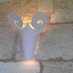 An einer Wand aus hellen Ziegeln hängt eine weiße Gipslampe in Form eines Ziegenkopfs