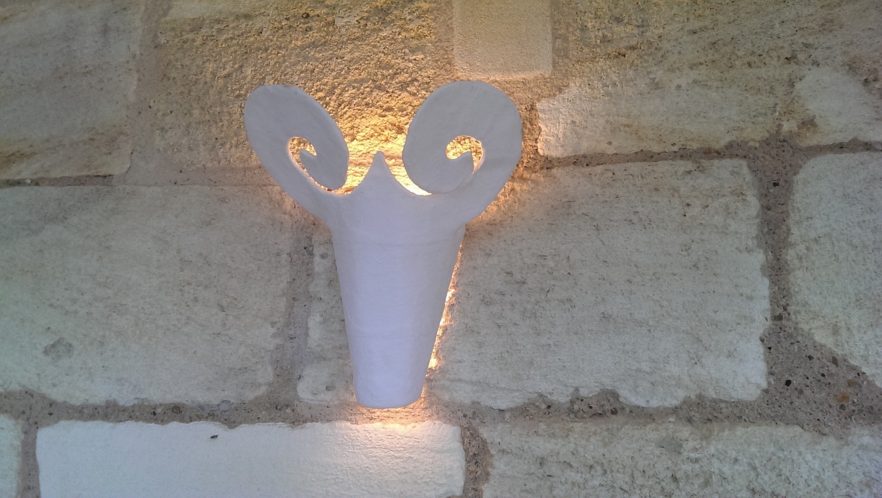 An einer Wand aus hellen Ziegeln hängt eine weiße Gipslampe in Form eines Ziegenkopfs
