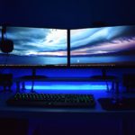 Eine blaue PC-Beleuchtung mit LEDs im Dunkeln. Man sieht zwei Monitore, eine Tastatur und eine Maus.