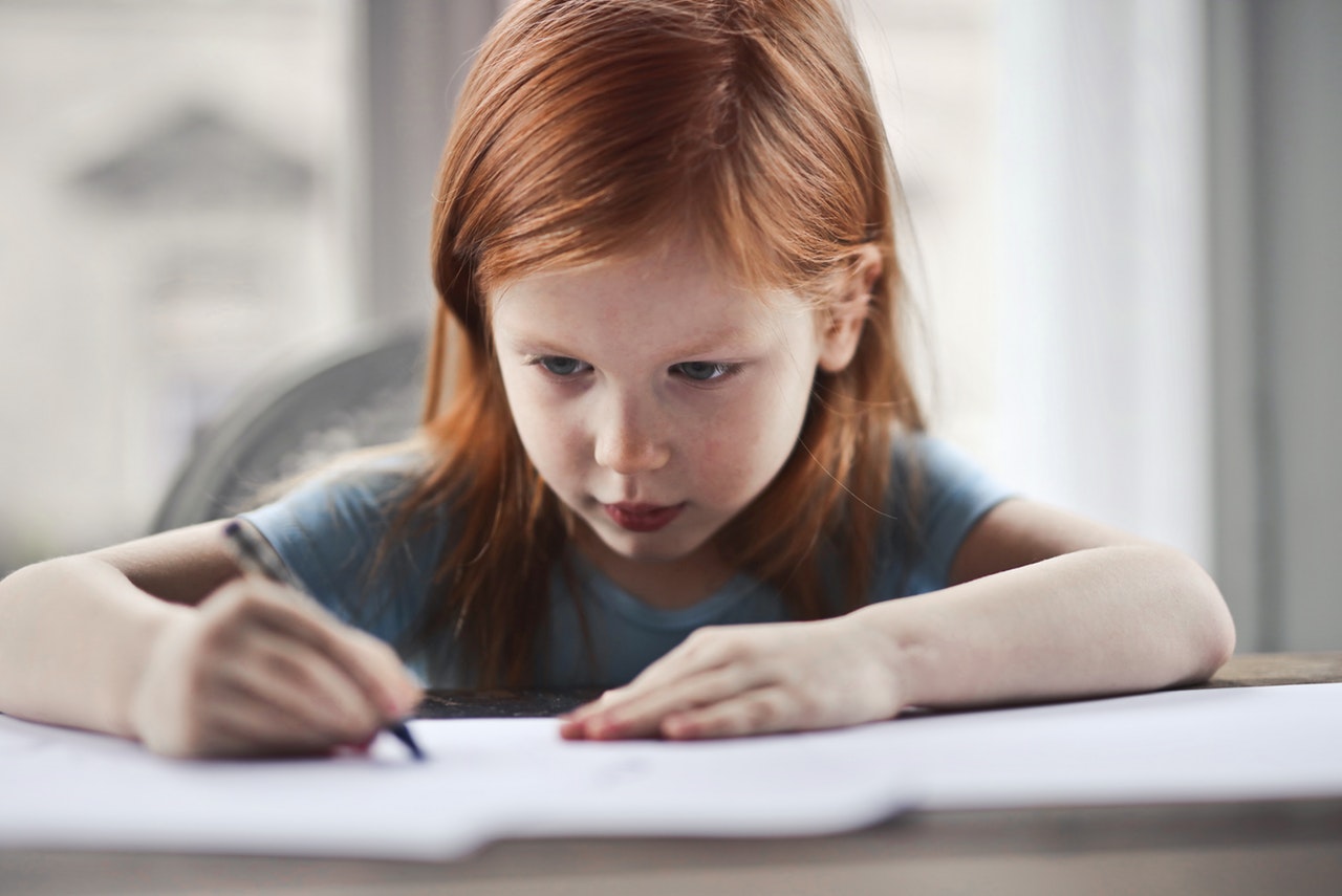 Rothaariges Kind schreibt konzentriert unter einer Schreibtischleuchte