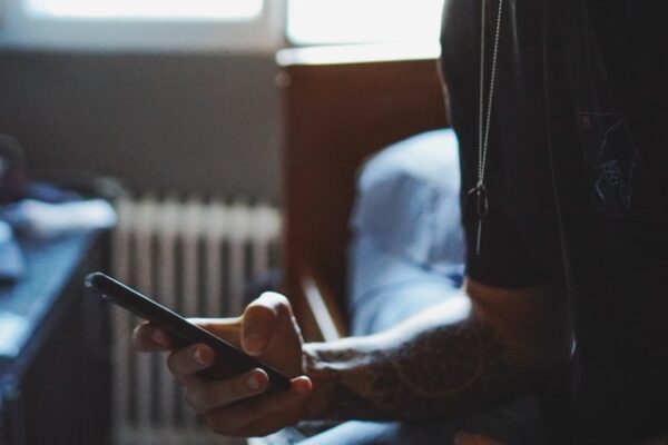 Jemand sitzt auf einem Bett und hält ein Smartphone in der Hand