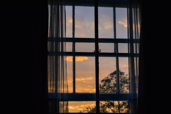 Durch ein halb geöffnetes Fenster sieht am einen Sonnenaufgang am Himmel