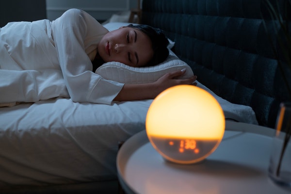 Eine Frau schläft in ihrem Bett, während der Tageslichtwecke langsam zu leuchten beginnt