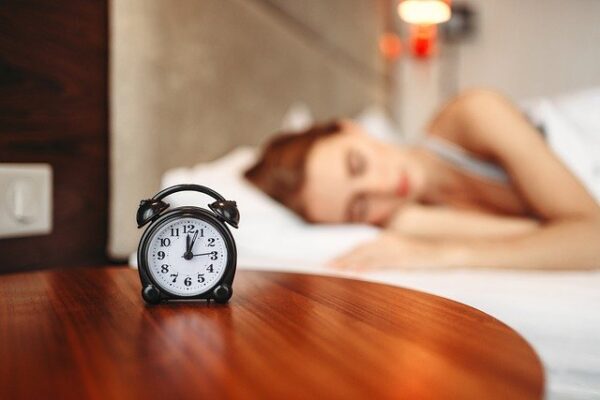 Eine Frau liegt schlafend im Bett, auf ihrem Nachttisch steht ein kleiner Wecker