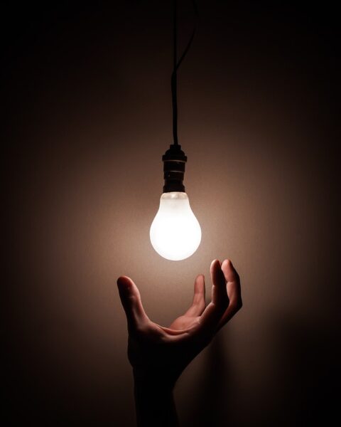 Eine Hand kommt von unten, um eine leuchtende Glühlampe zu berühren