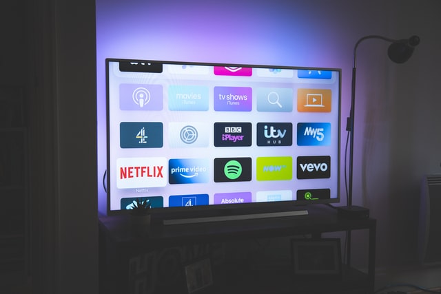 Ein Fernseher mit verschiedenen Apps auf dem Bildschirm. Die Wand dahinter ist sanft beleuchtet.