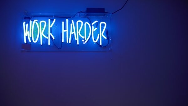 Ein blaues Neonschild mit den Worten Work Harder