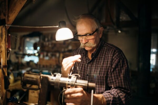Ein Mann mit Sicherheitsbrille arbeitet mit Drahtseil. Eine Lampe spendet Licht.