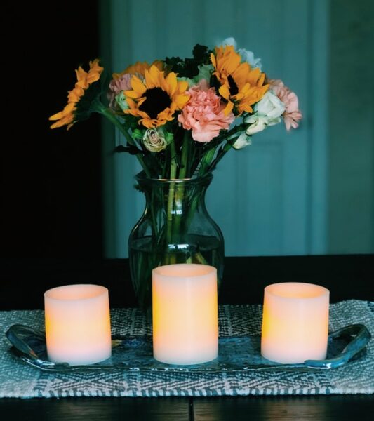 Drei elektrische Kerzen stehen vor einem Blumenstrauß