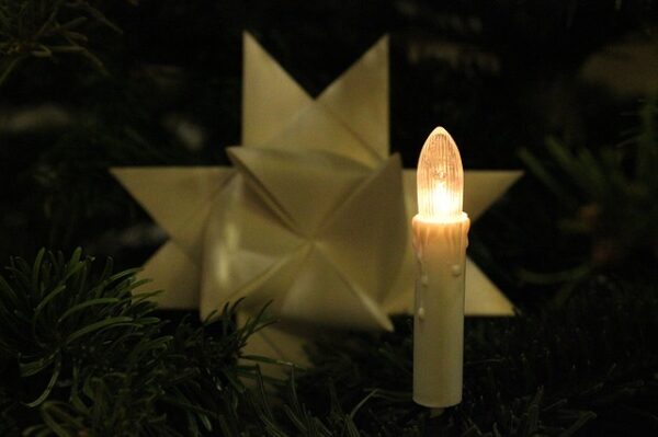 Eine elektrische Kerze vor einem gefalteten Papierstern auf einem Weihnachtsbaum