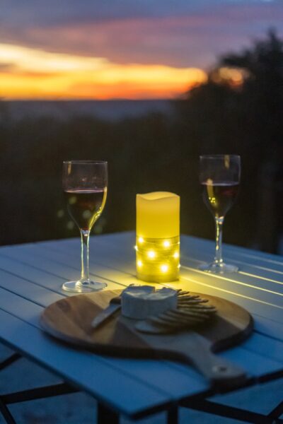 Eine elektrische Kerze mit Lichterkette auf einem Tisch mit zwei Weingläsern und einem Brett mit Käse