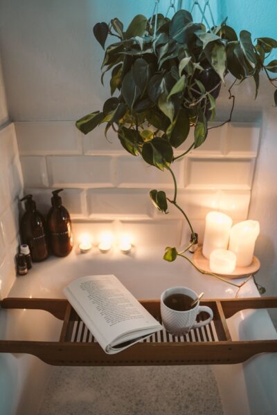 Badewanne mit Buch, Tasse und Kerzen sowie einer Pflanze und Pflegeprodukten