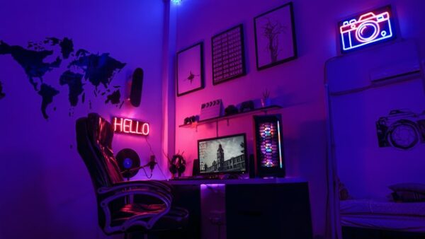 Ein Schreibtisch der von hinten mit LED beleuchtet wird, sowie ein leuchtender Bidlschirm, PC und Bilder an der Wand