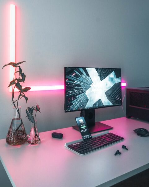 Hinter einem Bildschirm auf einem Schreibtisch wurde eine rosafarbene L-förmige LED-Leiste angebracht