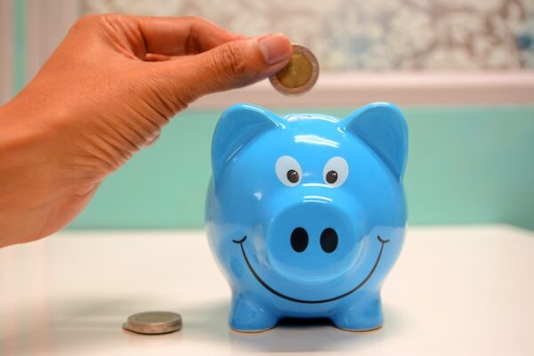 Jemand steckt Geldstücke in ein blaues, freundlich guckendes Sparschwein
