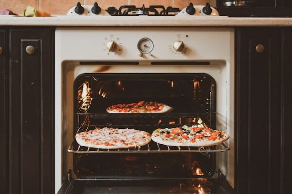 Ein geöffneter Ofen mit insgesamt 3 Pizzen auf Rost und Backblech